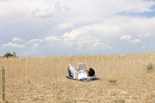 Chico joven leyendo un libro en el campo con nubes © ricardomoratilla