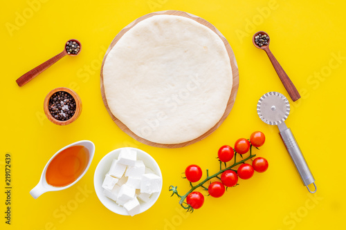 Ingredients for cooking pizza. Rolled out pizza dough, cherry tomatoes, olive oil, cheese mozzarella, spices on yellow background top view mockup