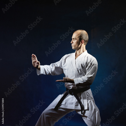 On a dark blue background, an adult sports a formal karate exercise