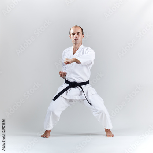 On a light background, an adult sportsman trains a formal karate exercise in a white karategi