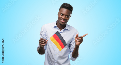 Young african american man holding german flag very happy pointing with hand and finger to the side