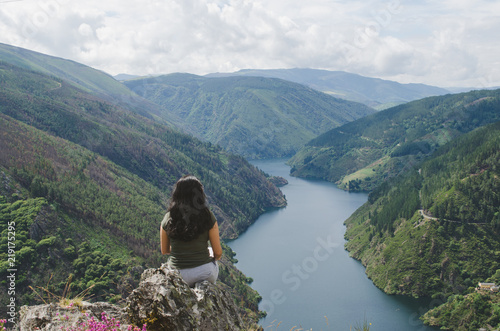 Woman sitting looking at landscape. Reservoir and mountains.