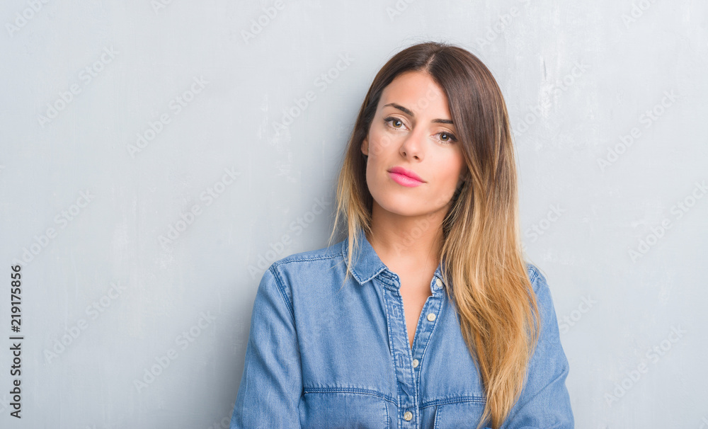Young adult woman over grey grunge wall wearing denim outfit with a confident expression on smart face thinking serious Young adult woman over grey grunge wall wearing denim outfit with a confident expression on smart face thinking serious