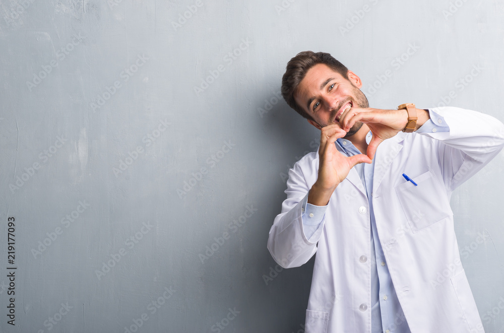 Handsome young professional man over grey grunge wall wearing white coat smiling in love showing heart symbol and shape with hands. Romantic concept. Handsome young professional man over grey grunge wall wearing white coat smiling in love showing heart symbol and shape with hands. Romantic concept.