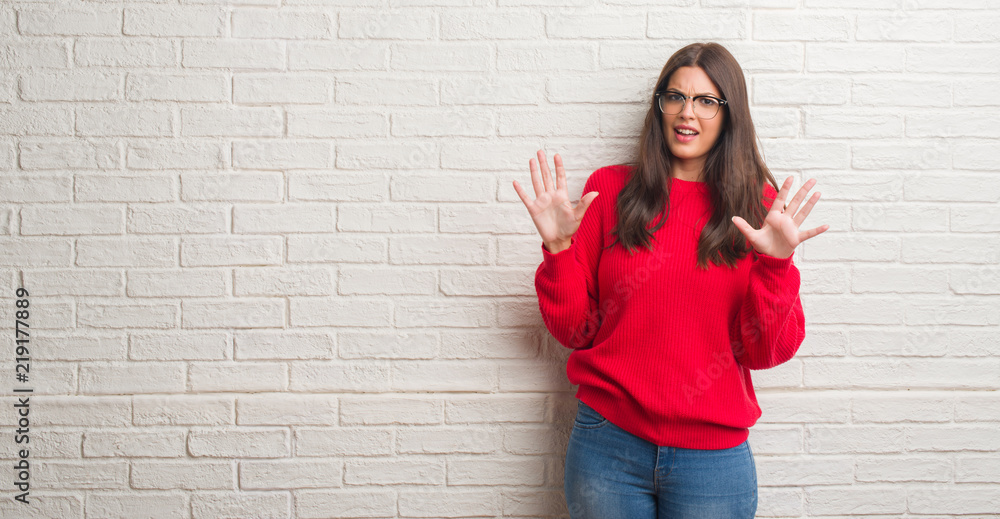 Young brunette woman standing over white brick wall afraid and terrified with fear expression stop gesture with hands, shouting in shock. Panic concept. Young brunette woman standing over white brick wall afraid and terrified with fear expression stop gesture with hands, shouting in shock. Panic concept.