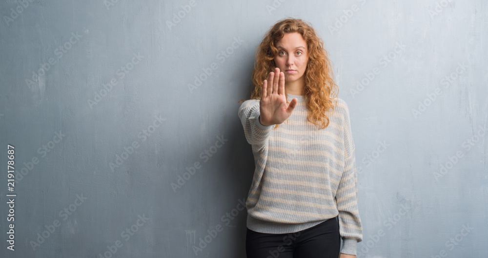 Fototapeta premium Young redhead woman over grey grunge wall doing stop sing with palm of the hand. Warning expression with negative and serious gesture on the face.