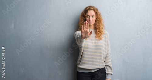 Young redhead woman over grey grunge wall doing stop sing with palm of the hand. Warning expression with negative and serious gesture on the face. © Krakenimages.com