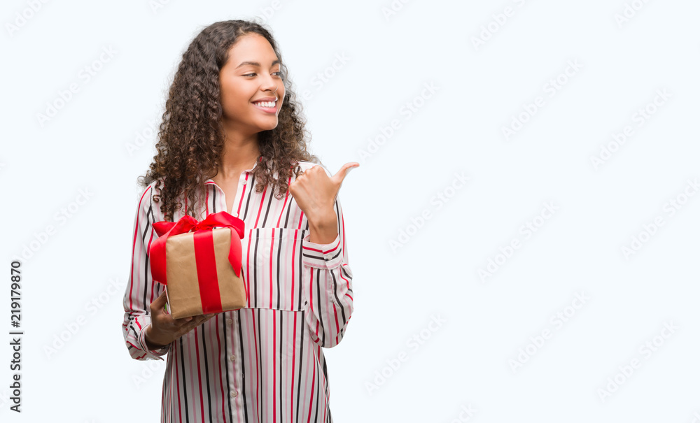 Young hispanic woman in love holding present pointing and showing with thumb up to the side with happy face smiling Young hispanic woman in love holding present pointing and showing with thumb up to the side with happy face smiling