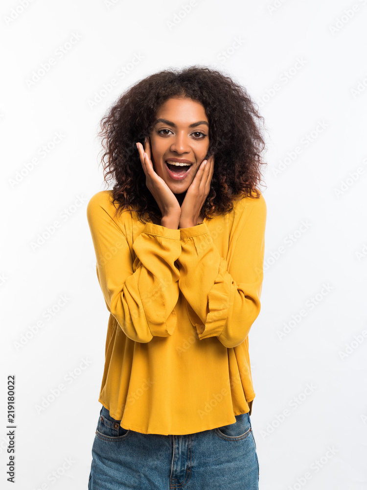 Beautiful african american woman with afro hair in yellow wear smiling, pleasantly surprised to camera over white wall background. Cute mixed race girl's portrait with amazement Beautiful african american woman with afro hair in yellow wear smiling, pleasantly surprised to camera over white wall background. Cute mixed race girl's portrait with amazement