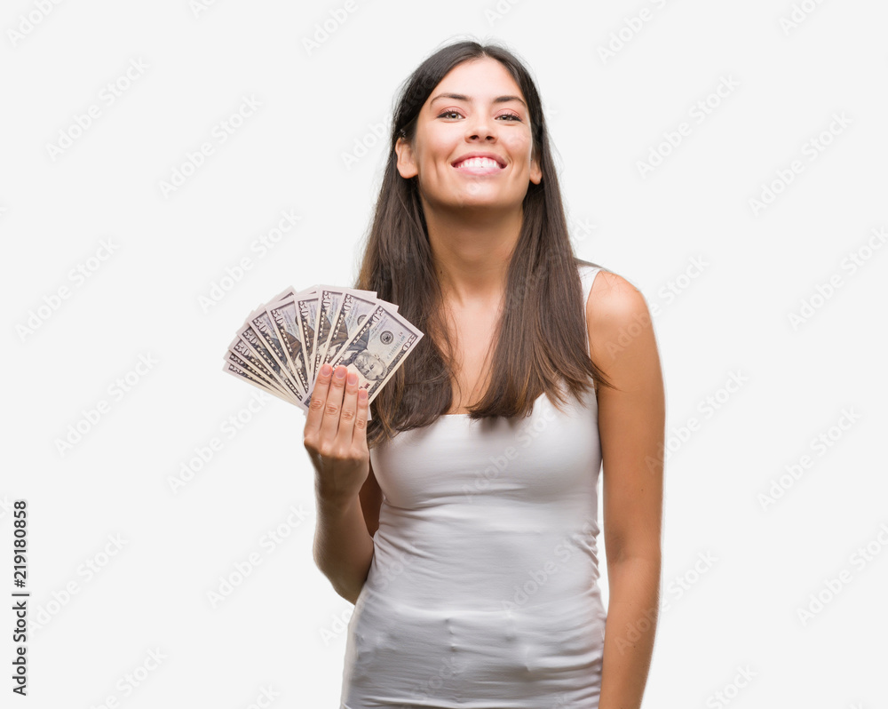 Young hispanic woman holding dollars with a happy face standing and smiling with a confident smile showing teeth Young hispanic woman holding dollars with a happy face standing and smiling with a confident smile showing teeth