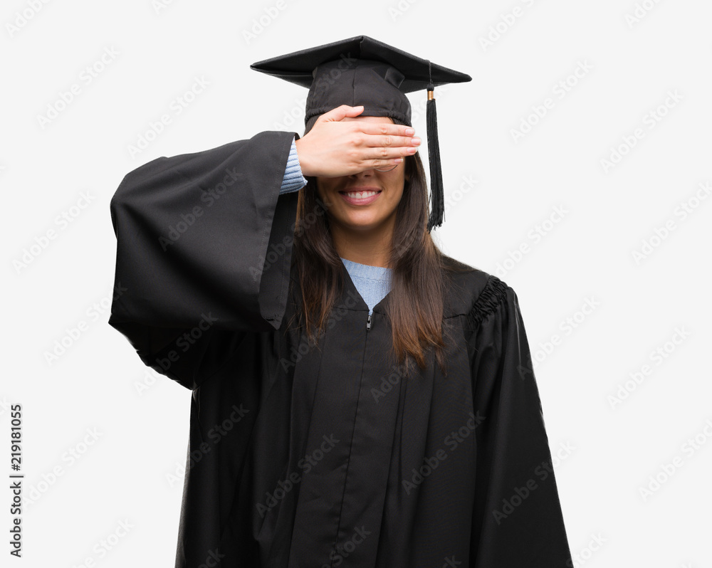 Young hispanic woman wearing graduated cap and uniform smiling and laughing with hand on face covering eyes for surprise. Blind concept. Young hispanic woman wearing graduated cap and uniform smiling and laughing with hand on face covering eyes for surprise. Blind concept.