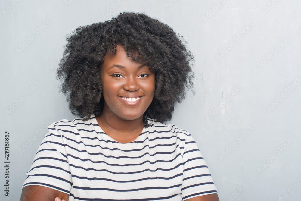 Young african american plus size woman over grey grunge wall happy face smiling with crossed arms looking at the camera. Positive person. Young african american plus size woman over grey grunge wall happy face smiling with crossed arms looking at the camera. Positive person.