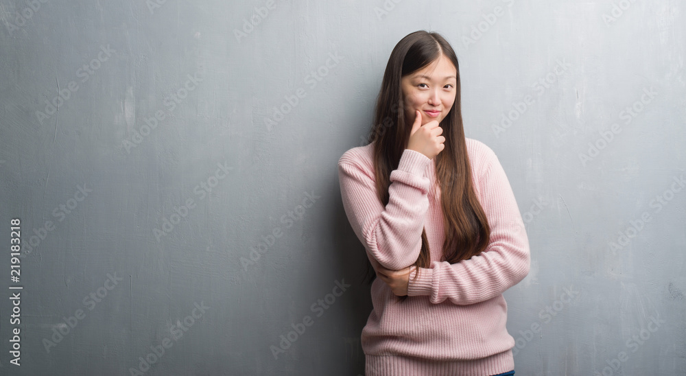 Young Chinese woman over grey wall looking confident at the camera with smile with crossed arms and hand raised on chin. Thinking positive. Young Chinese woman over grey wall looking confident at the camera with smile with crossed arms and hand raised on chin. Thinking positive.