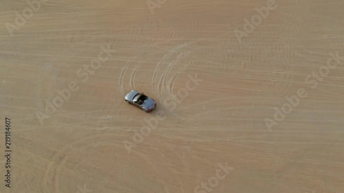 Grey convertible car filmed from distant above while making 8 circles in the sand. photo