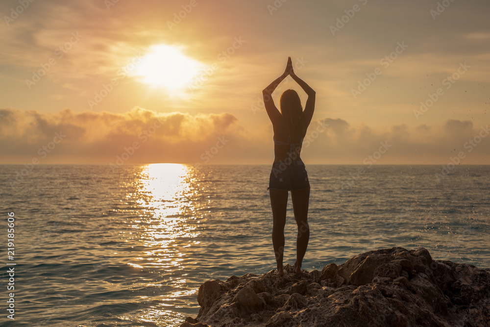 Beautiful young woman doing yoga on a rock by the beach