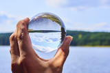 Hand holding a glass ball reflecting the lake and the forest. Concept of environment, nature protection, ecology. Selective focus