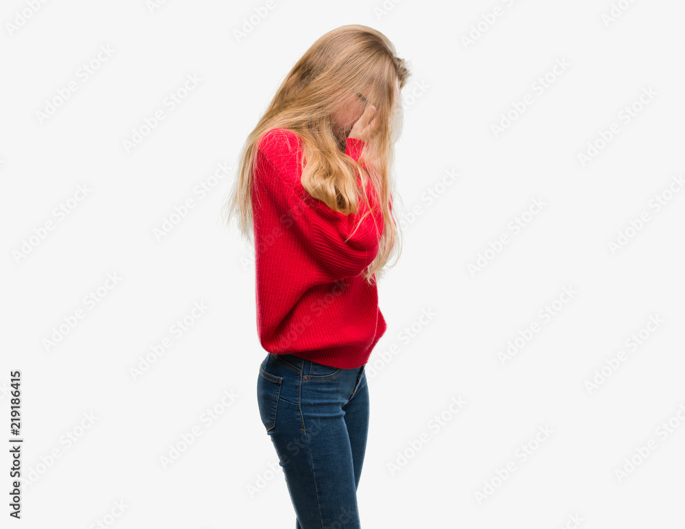 Blonde teenager woman wearing red sweater with sad expression covering face with hands while crying. Depression concept. Blonde teenager woman wearing red sweater with sad expression covering face with hands while crying. Depression concept.