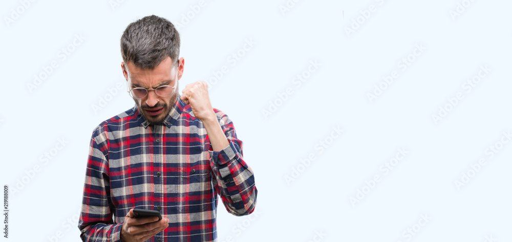 Young hipster adult man holding smartphone annoyed and frustrated shouting with anger, crazy and yelling with raised hand, anger concept Young hipster adult man holding smartphone annoyed and frustrated shouting with anger, crazy and yelling with raised hand, anger concept