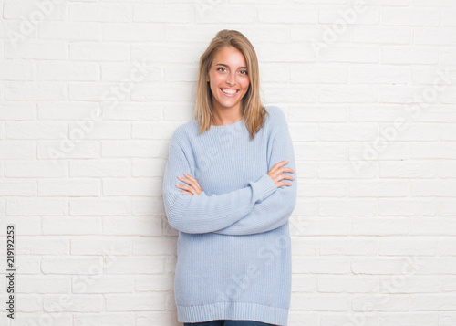 Beautiful young woman over white brick wall happy face smiling with crossed arms looking at the camera. Positive person.