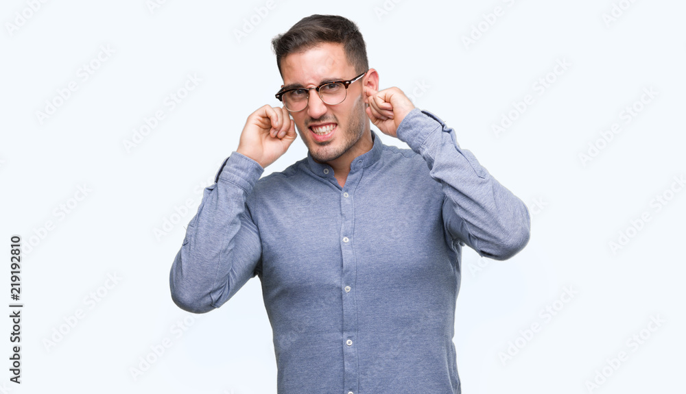 Handsome young elegant man wearing glasses covering ears with fingers with annoyed expression for the noise of loud music. Deaf concept. Handsome young elegant man wearing glasses covering ears with fingers with annoyed expression for the noise of loud music. Deaf concept.