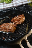 Fragment of grill pan with two slices steak in an iron pan with herbs and spices. Food concept