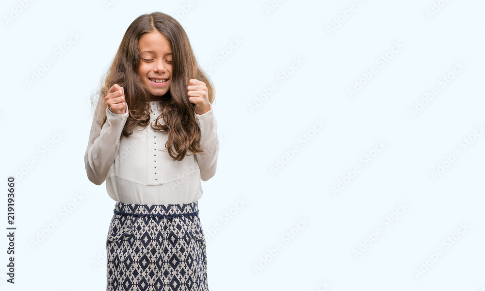 Brunette hispanic girl excited for success with arms raised celebrating victory smiling. Winner concept. Brunette hispanic girl excited for success with arms raised celebrating victory smiling. Winner concept.