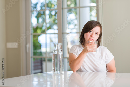 Down syndrome woman at home drinking water with a confident expression on smart face thinking serious