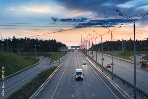 Highway traffic in sunset. minivan on the asphalt road with metal safety barrier or rail. Pine forest on the background