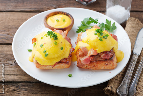 Eggs benedict with bacon on wooden background . 