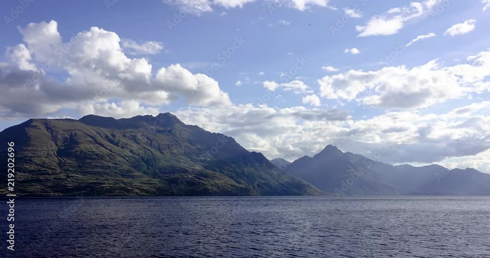 Time-lapse of mountains by the sea in Queenstown New Zealand. Moving clouds on blue sky and massive hills and water in picturesque timelapse. Time-lapse of mountains by the sea in Queenstown New Zealand. Moving clouds on blue sky and massive hills and water in picturesque timelapse.