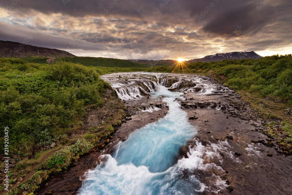Large waterfall in a wide landscape with evening light, sunset with rays on a mountain range, water movement in long exposure - Location: Iceland, Golden circle, Bruarfoss Large waterfall in a wide landscape with evening light, sunset with rays on a mountain range, water movement in long exposure - Location: Iceland, Golden circle, Bruarfoss