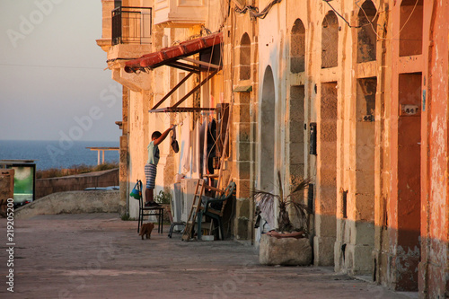 Real life on Malta see side during orange sunset - boy hanging clothes drying, two washing machines and gignger cat on the street photo