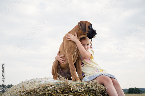 Young dog with little girl sitting  on top of haystack.