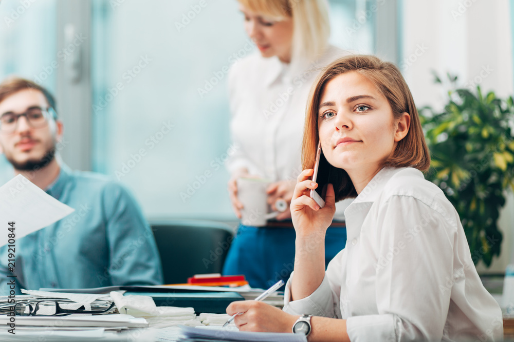 Obraz premium Young woman at the office talking on phone with team in background