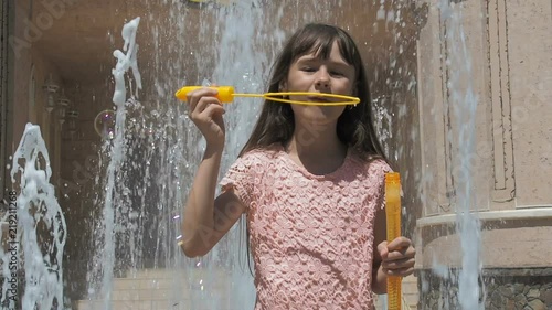 A child with soap bubbles near the fountain. Little girl is playing with soap bubbles against the background of a fountain. photo