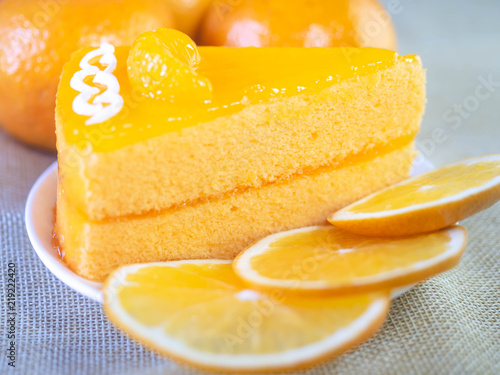 Orange cake on white dish and wooden fork is on table.
