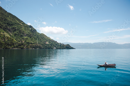 Lone traditional fisherman collects his nets from a small canoe on the blue, tranquil beauty of Lake Atitlán in Guatemala