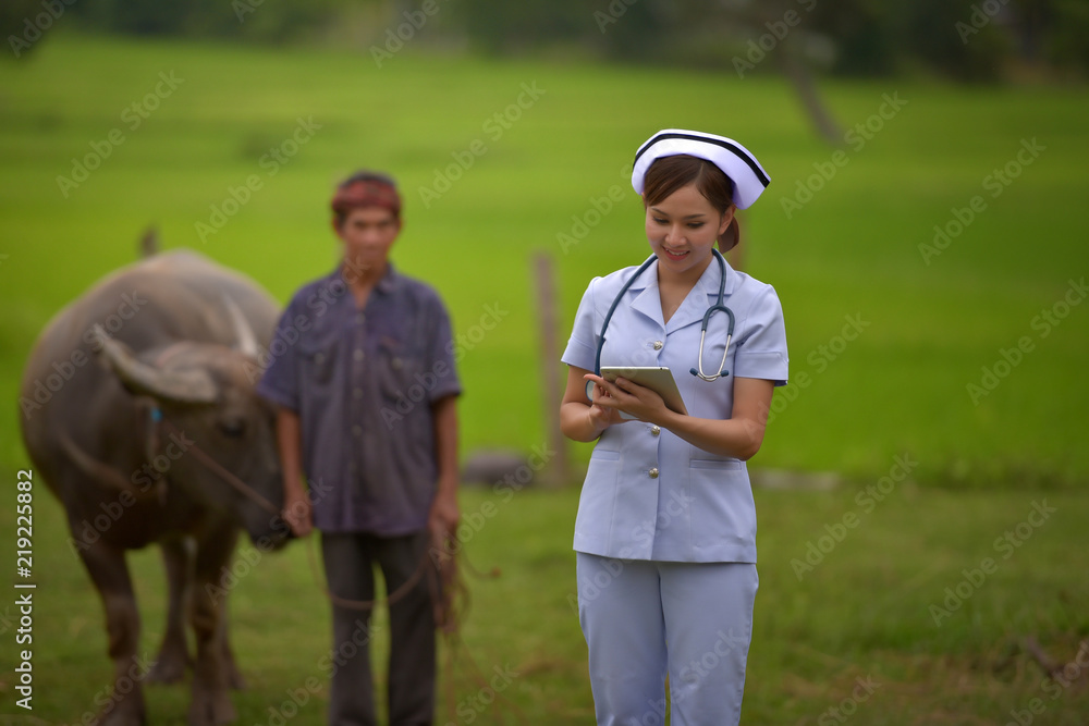 Beautiful nurse smiling and holding a tablet with headphones standing behind the Asian peasant.