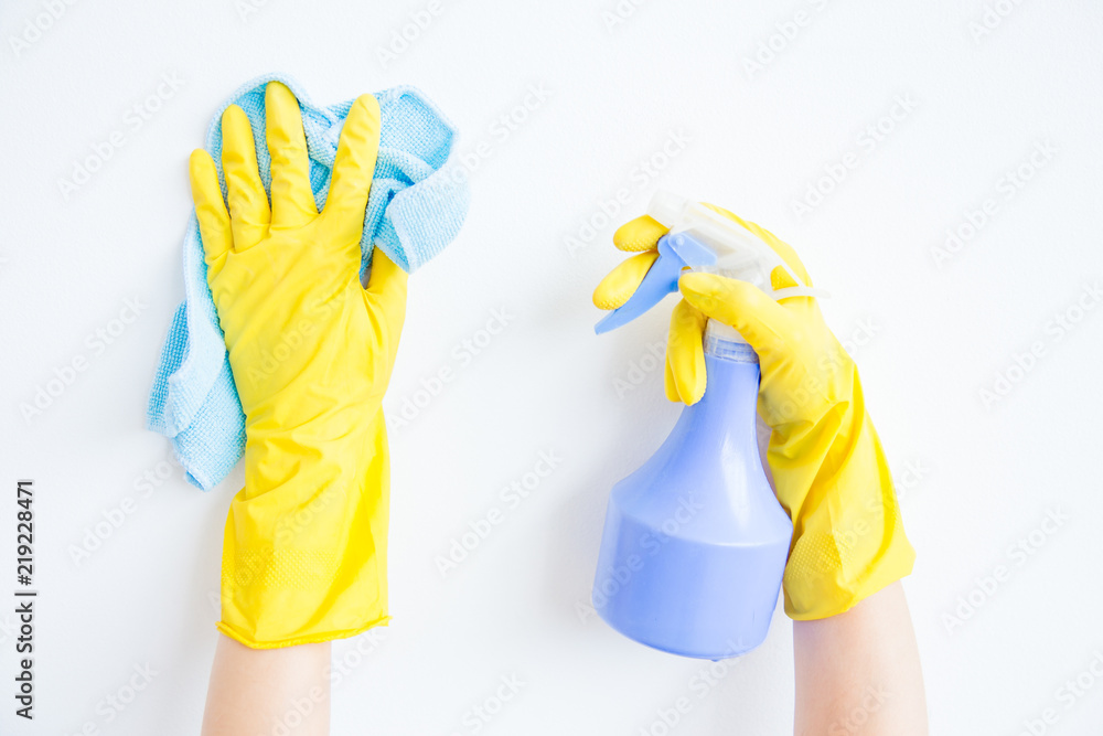 Woman in protective gloves is smiling and wiping dust using a spray and a duster Woman in protective gloves is smiling and wiping dust using a spray and a duster