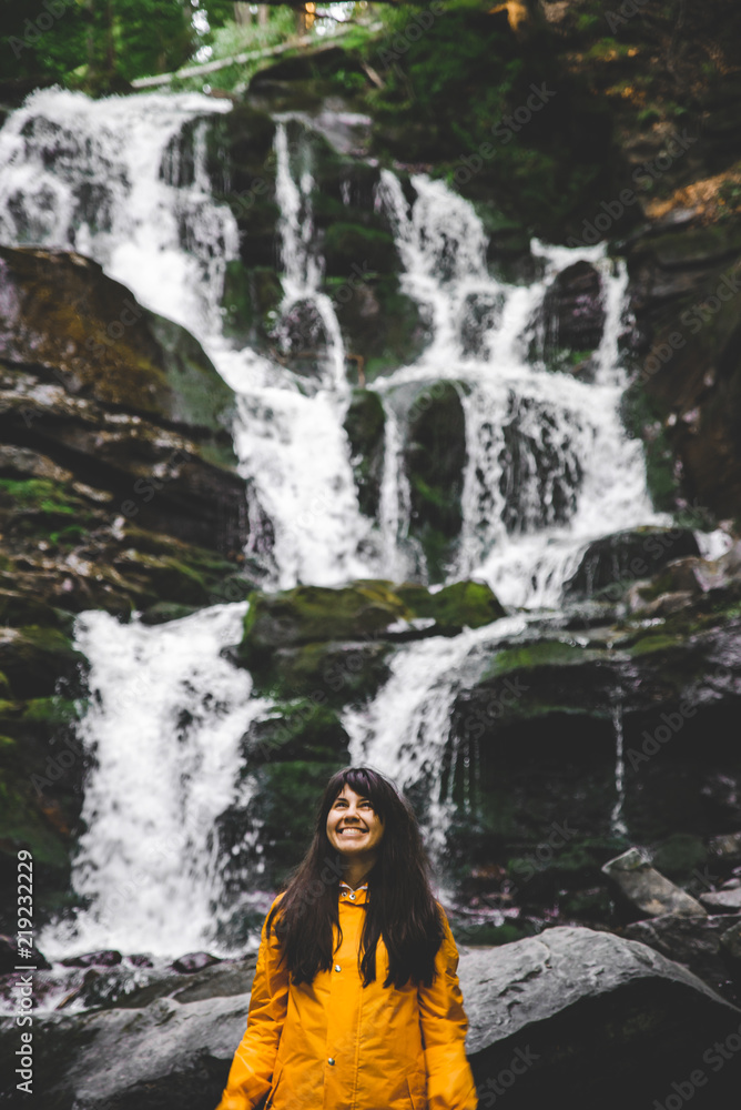 smiling woman in yellow raincoat with waterfall on background