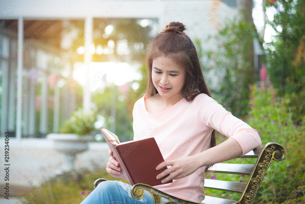 Fototapeta premium Beautiful asian girl sitting on bench reading book in park