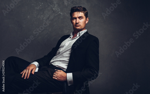Handsome man in a business suit sits on a chair and looks away, portrait