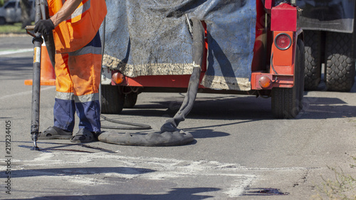 Workers repair the road, pour small cracks with bitumen to prevent further destruction of the road surface