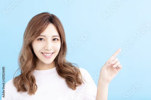 Obraz na plátně smiling Young woman pointing at blue background