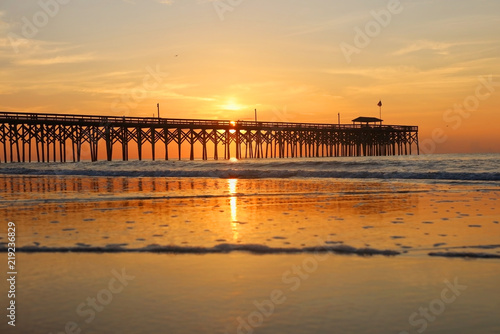 Cloudy sunrise over Atlantic ocean. Beautiful marine landscape with sun rising over calm atlantic ocean beach with wooden pier. South Carolina, Myrtle Beach area, USA. Vacation background.