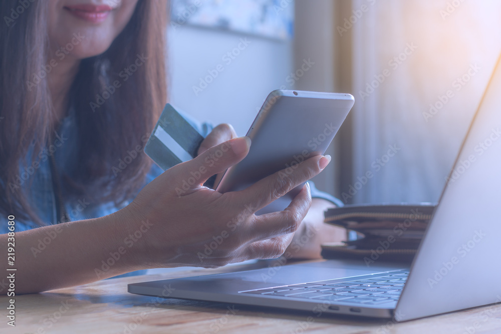 Woman hand holding credit card and using mobile smartphone for online shopping and payment, m-banking, work on the wooden table at Woman hand holding credit card and using mobile smartphone for online shopping and payment, m-banking, work on the wooden table at