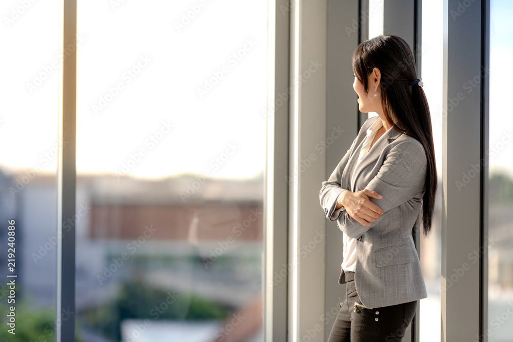 Fototapeta premium Asian long-haired businesswoman looks good in a suit stand with confidence in the office window.