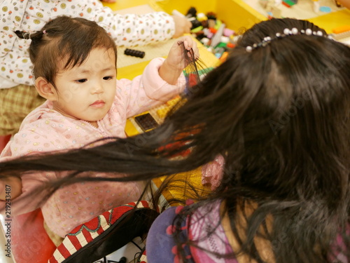 Little Asian baby girl, 17 months old, enjoys playing her mother's hairs