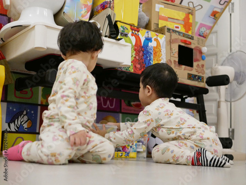 Asian baby, 31 months old, (right) is cleaning up / putting away toys she played with her little sister photo