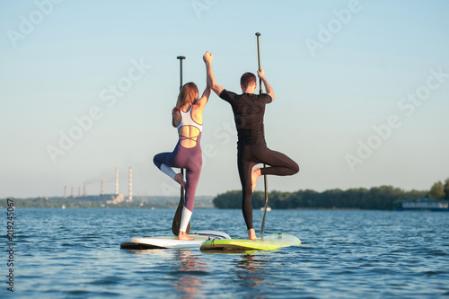 couple practicing yoga on the river stand up paddle